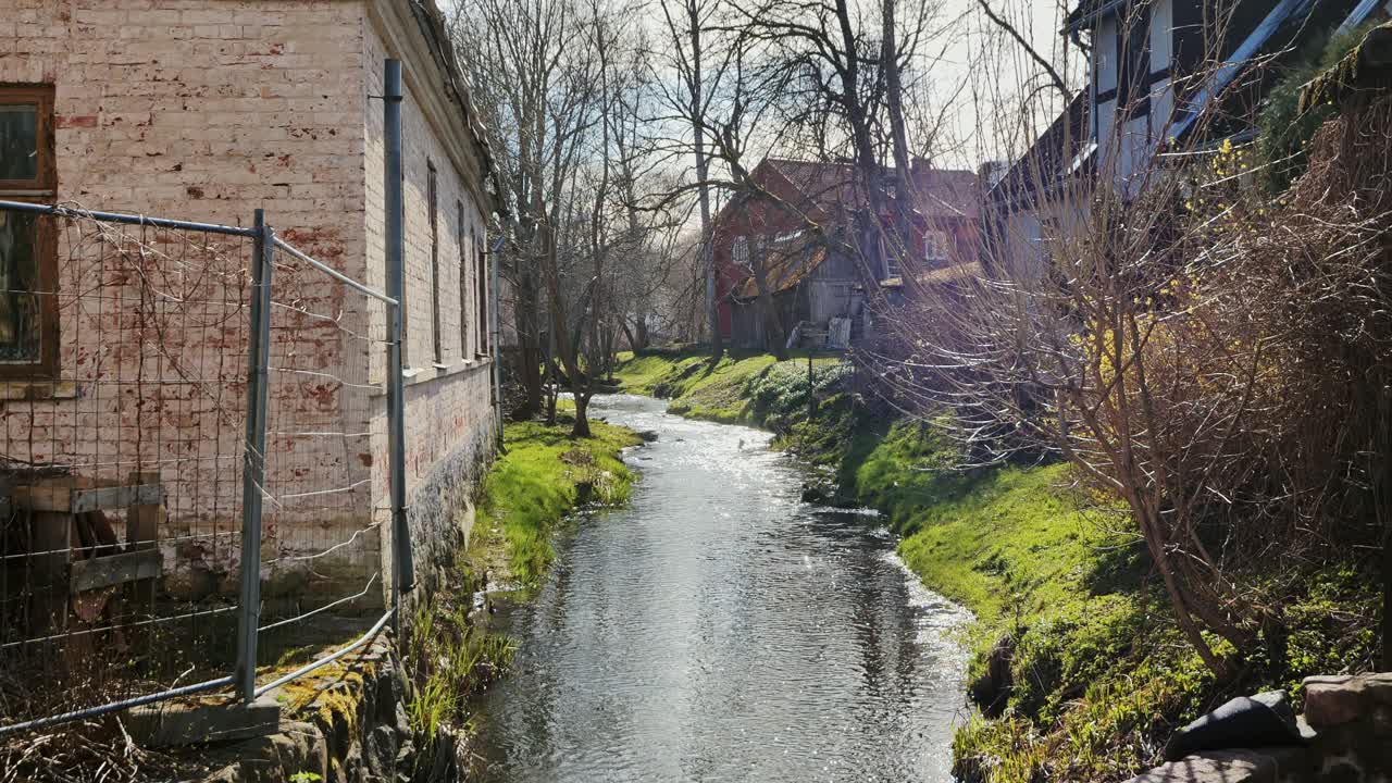 Idyllic Latvian creek flowing calmly by homes, rich historic character, Kuldiga