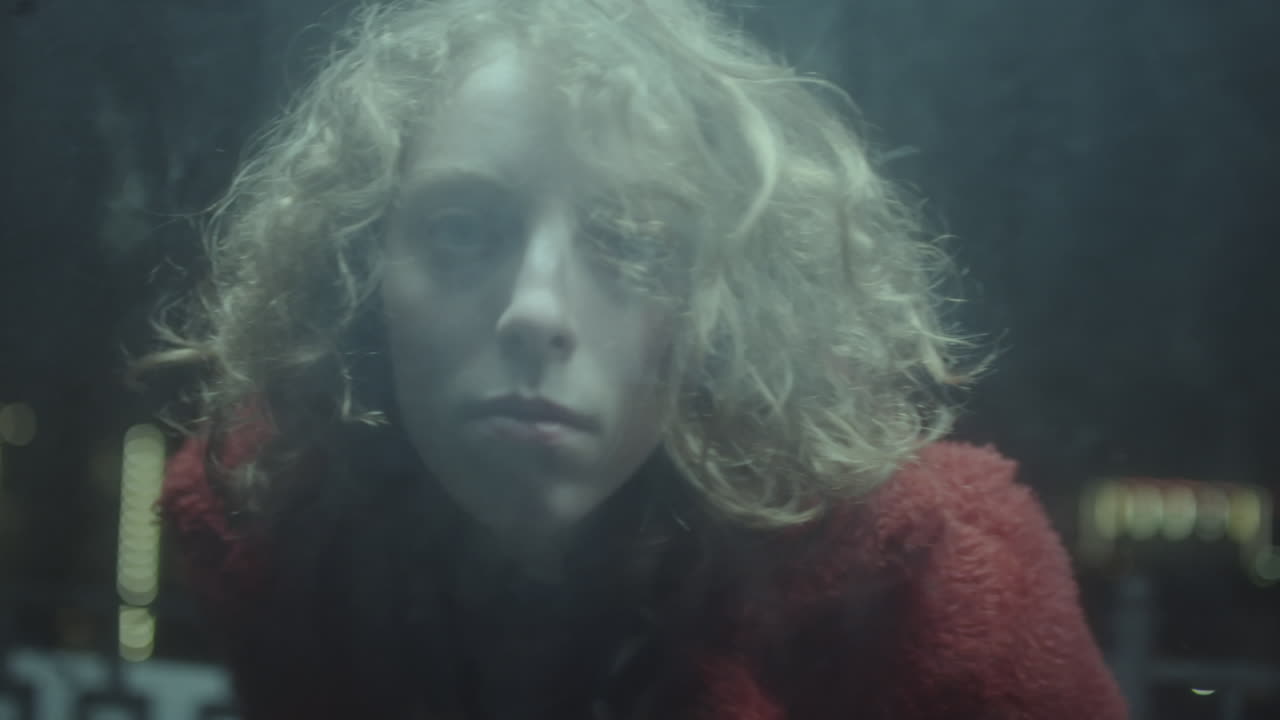 Young Woman Looking at Camera through Glass at Night