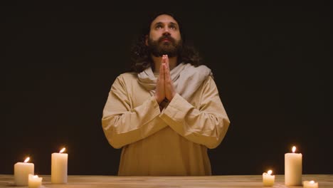 studio shot of man wearing robes representing figure of jesus christ praying at altar