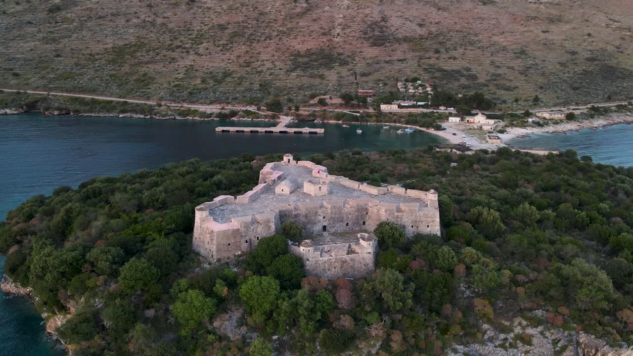 vista aérea de la órbita del castillo vacío de ali pasha con amanecer dorado sobre enormes montañas en la bahía de porto palermo, albania