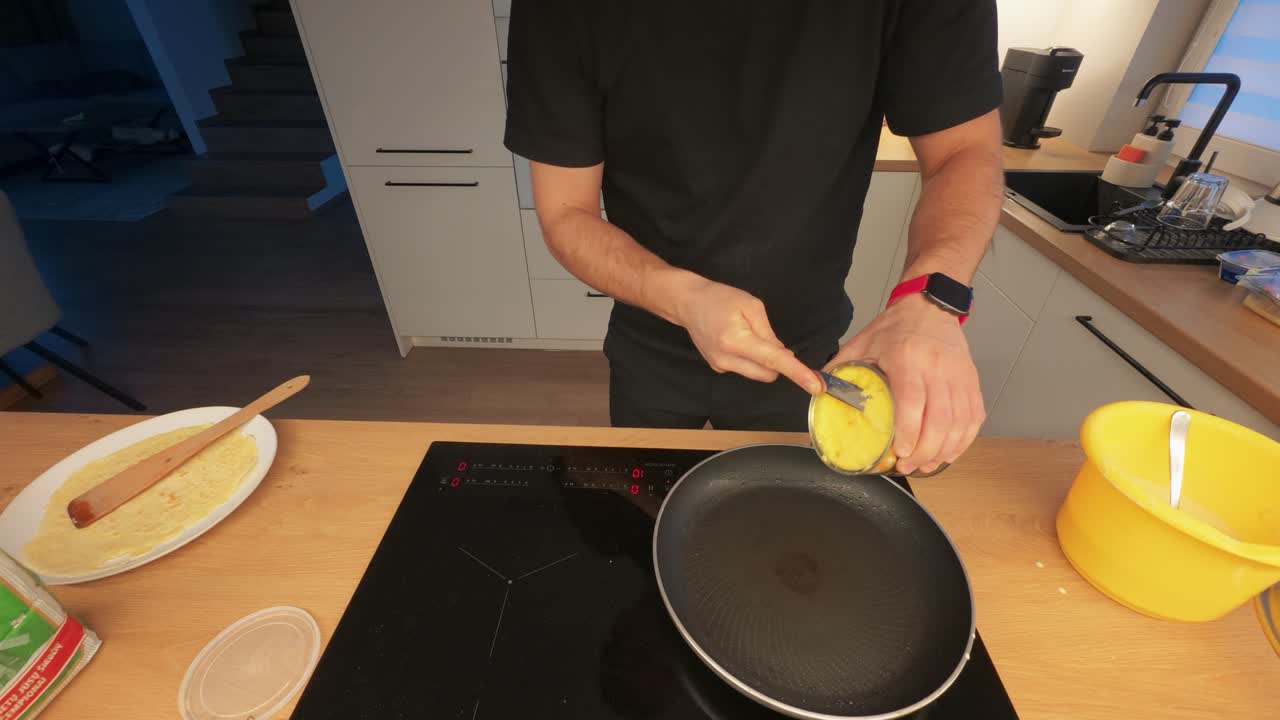 A home cook expertly flips a crepe on an induction stove in a modern kitchen. The scene captures the precision and skill involved in cooking. Warm lighting enhances the inviting atmosphere