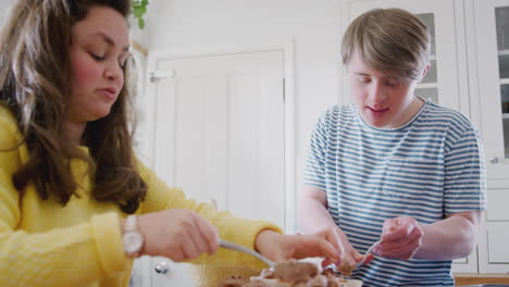pareja con síndrome de down decorando cupcakes caseros con glaseado en la cocina en casa