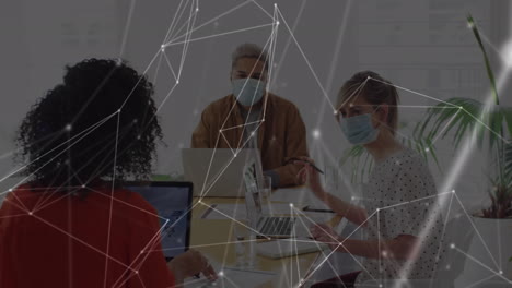 Animation of network over male and female creative colleagues in face masks working in office