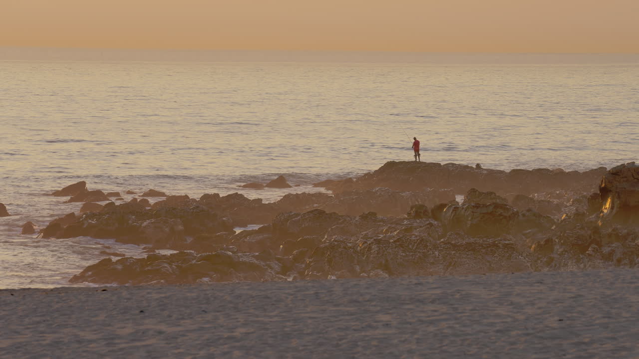 일출 동안 바다에서 낚시하는 어부의 실루엣