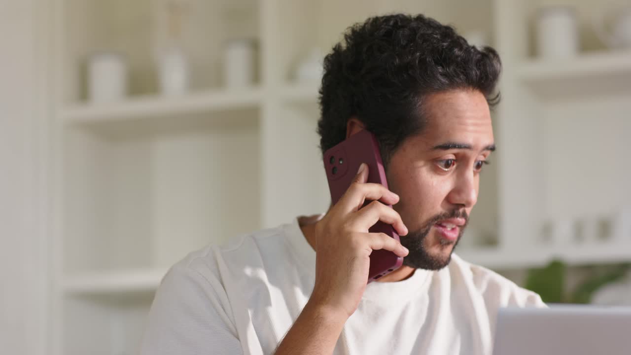 Pria Afrika-Amerika mengangkat telepon ungu yang berdering sambil membaca laptop di kantor rumah untuk bekerja