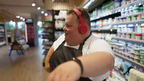 happy male supermarket worker with overweight white t-shirt and black front in red headphones is happy dancing and walking along the milk aisles in the supermarket