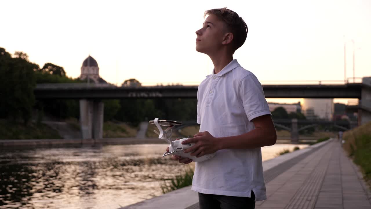 해가 지는 강 근처에서 드론을 조종하는 어린 소년