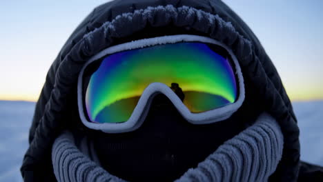 person in winter gear with snow goggles at sunrise in snowy mountains