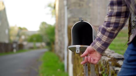 Man-checking-the-mail-in-an-empty-US-mail-box,-in-a-countryside-green-village