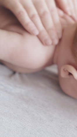 little boy with short fair hair lies on stomach on baby changing table and skilled nurse practices back massage closeup