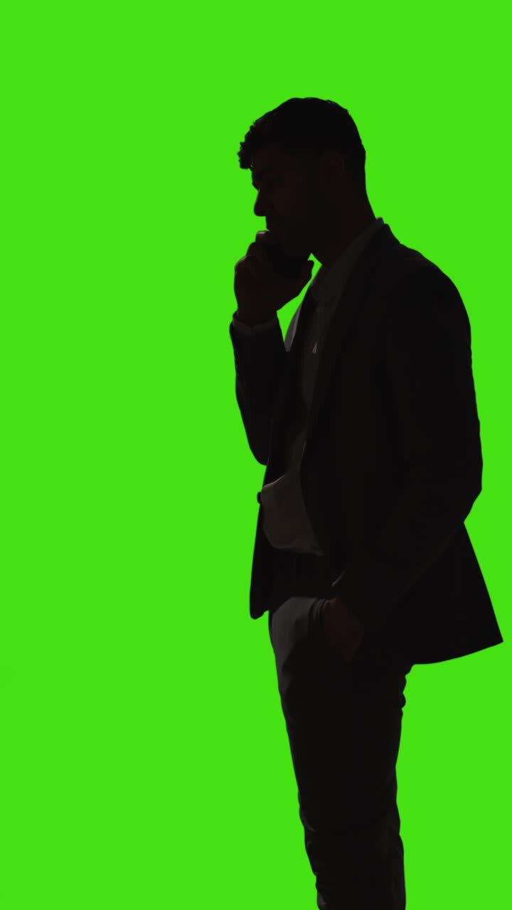 Video verticale: silhouette di un uomo d'affari in piedi che telefona al cellulare su sfondo green screen.