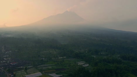 un campo brumoso en indonesia con el volcán merapi humeante en el fondo