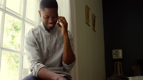 Front-view-of-young-black-father-talking-on-mobile-phone-with-baby-in-a-comfortable-home-4k