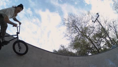 bmx biker riding by on top of pool bowl sideways, fisheye close tracking shot at 4k 800fps sunrise at the skatepark slow motion