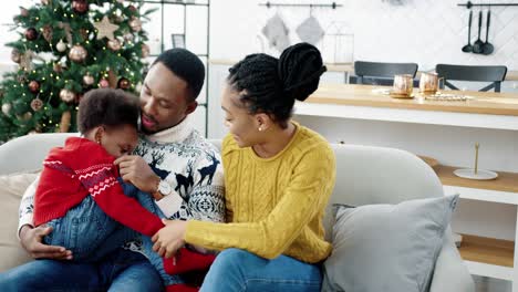 Porträt-Einer-Glücklichen-Familie,-Die-Zusammen-Heiligabend-Zu-Hause-In-Einem-Weihnachtlich-Dekorierten-Zimmer-Verbringt-Liebevolle-Mama-Und-Papa-Mit-Spielendem-Kind-Auf-Dem-Sofa-In-Der-Nähe-Des-Neujahrsbaums