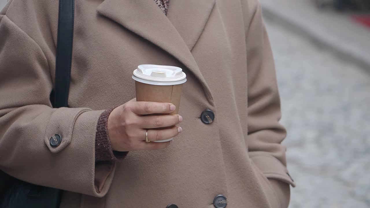 Persona in cappotto che tiene una tazza di caffè usa e getta all'aperto.
