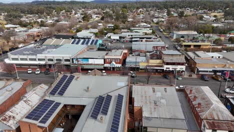 aerial footage pans above a small australian town’s main street, highlighting solar panels on rooftops, mixed-use buildings, and light daytime traffic