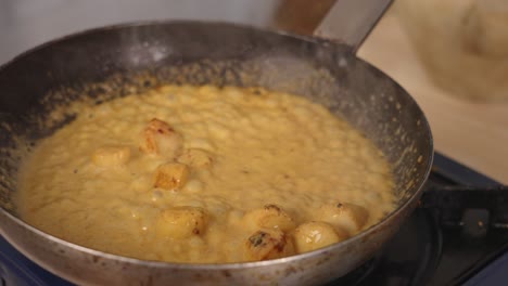 Delicious-creamy-coconut-curry-seafood-scallops-simmering-on-shallow-frying-pan-with-aromatic-smell,-close-up-shot-professional-chef-cooking-concept