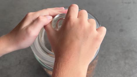 las manos de los niños luchan por abrir la tapa del tarro de galletas, así que se lleva el contenedor lleno