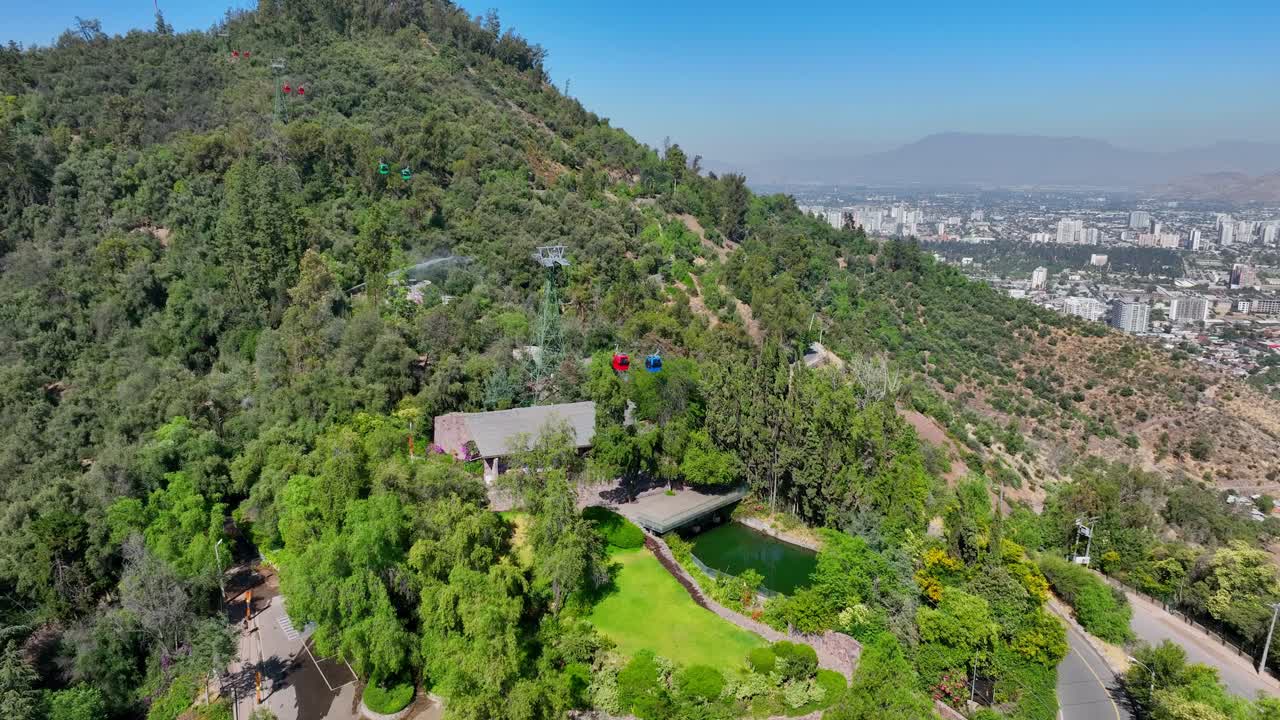 Orbit Drone Shot Around Lush Hillside of San Cristóbal Hill in Santiago, Featuring Cable Cars, Greenery, and Distant City Views