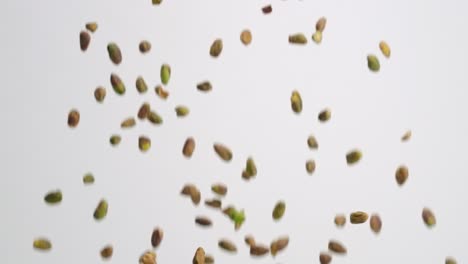 shelled pistachio nuts raining down on white backdrop in slow motion