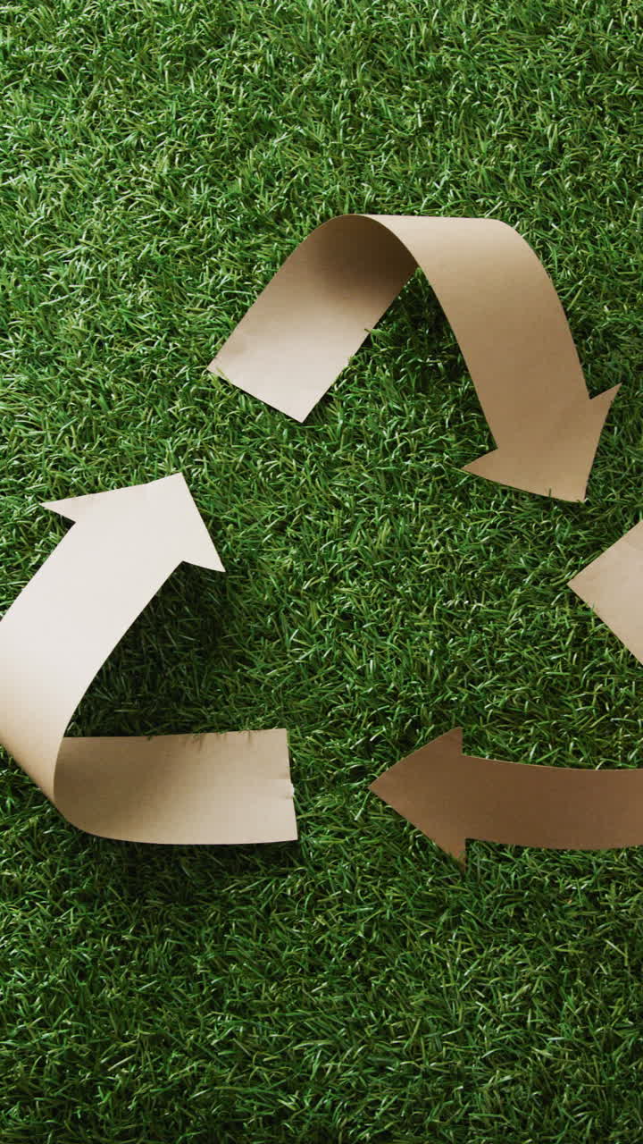 Vertical video of close up of recycling symbol of paper arrows with copy space on grass background