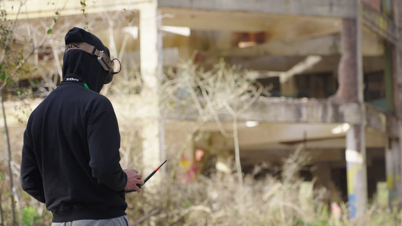 Uomo con occhiali FPV che pilota un drone con il telecomando vicino a un edificio abbandonato.