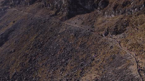 Fast-moving-drone-footage-captures-morning-in-Huancayo,-Peru,-as-citizens-briskly-walk-along-a-mountain-road-towards-Huaytapallana-mountain-for-the-Tayta-Shanti-festival