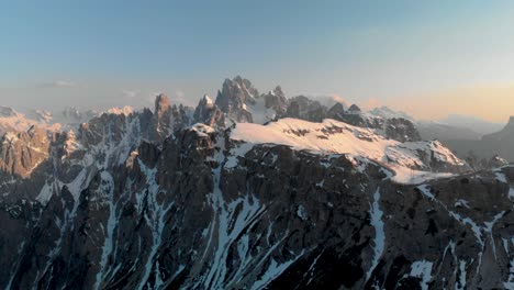 aerial 4k drone shot panning across snow-capped dolomites at sunset. stunning winter mountain landscape with golden hour light and dramatic alpine scenery.