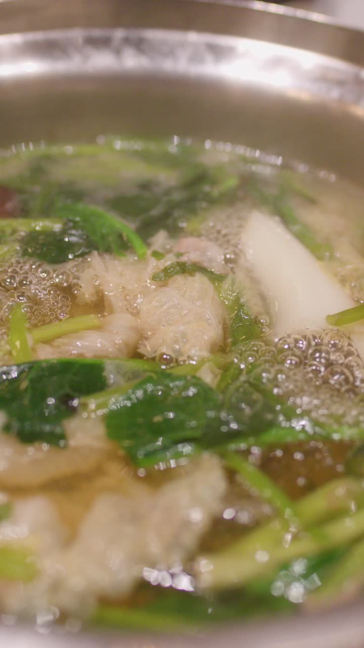Primo piano di brodo di hotpot bollente con verdure a foglia, carni assortite e verdure sotto un'illuminazione calda.