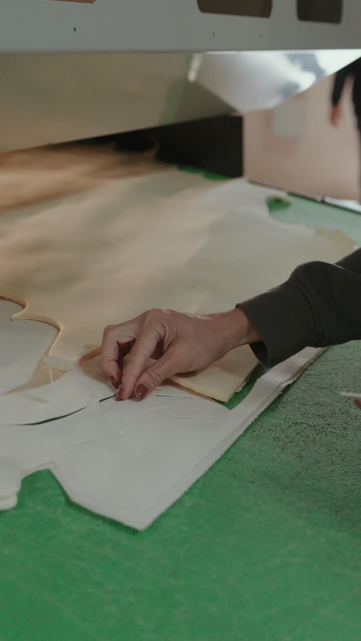 Vista vertical de unas manos recogiendo piezas cortadas de plantillas de cuero en una fábrica de zapatos