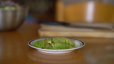 Close-up-of-adding-grates-pepper-on-a-sliced-​​avocado-on-a-plate