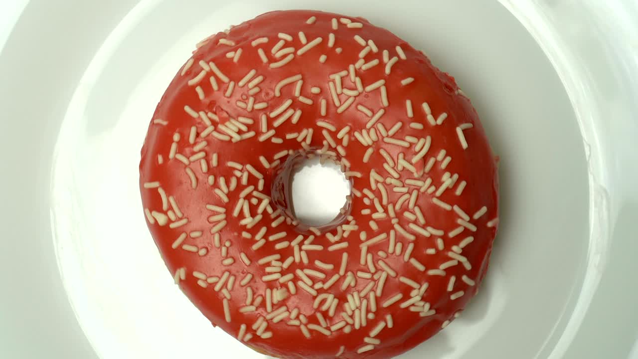 deliciosa rosquilla roja dulce girando en un plato. vista superior. cámara zoom en. brillante y colorido salpicado rosquilla primer plano macro disparo girando en una placa blanca.