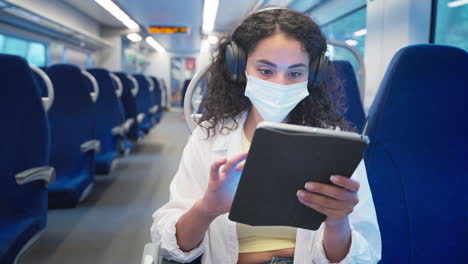 woman using tablet on a train wearing a mask and headphones