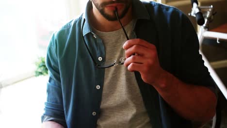 Thoughtful-man-holding-his-glasses-to-his-chin-while-having-coffee