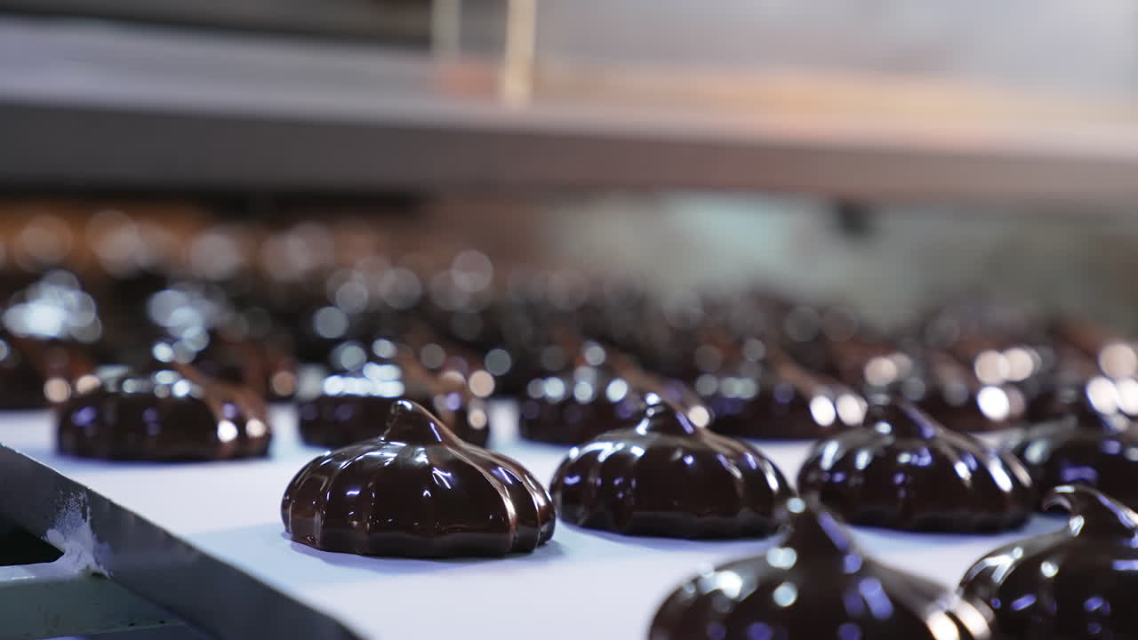 Zephyr candies coated in black chocolate. Ready-made chocolate desserts move on the conveyor belt. Close up.