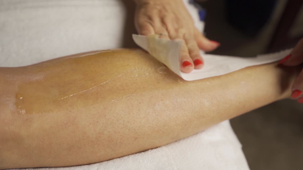 Depilazione con cera su gambe femminili, rallentatore, primo piano.