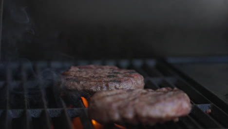 primer plano en cámara lenta de dos hamburguesas que chisporrotean en una barbacoa mientras las llamas naranjas se disparan desde abajo