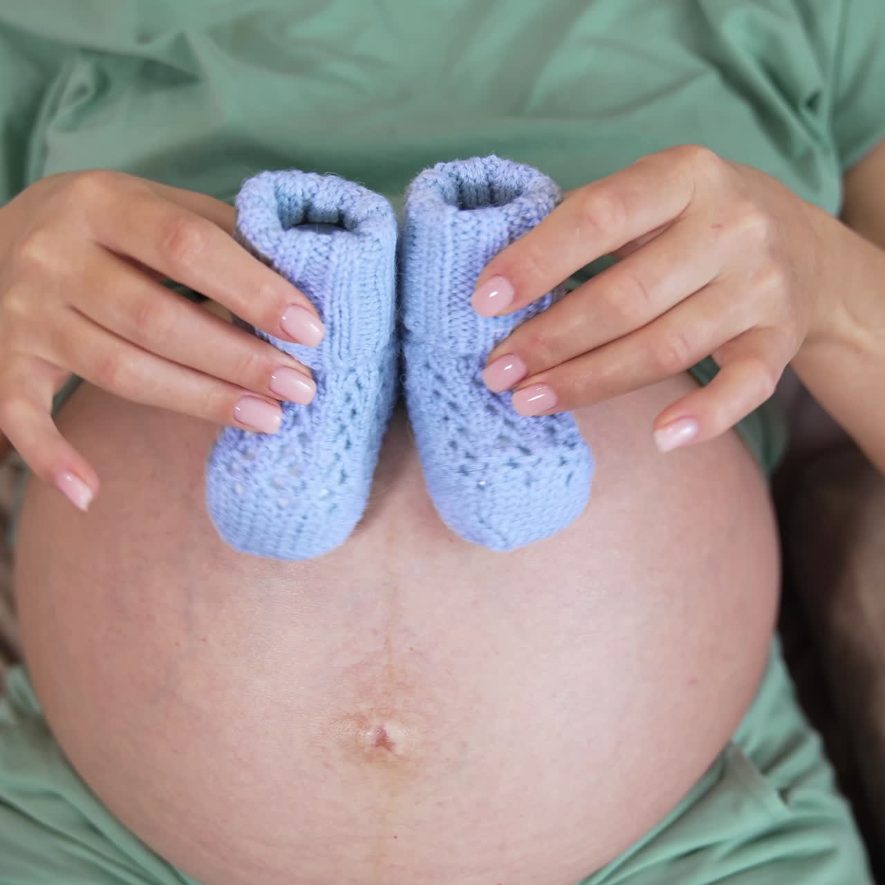 Pregnant woman belly with newborn baby booties. Pregnant woman with baby accessories on bed. Close up