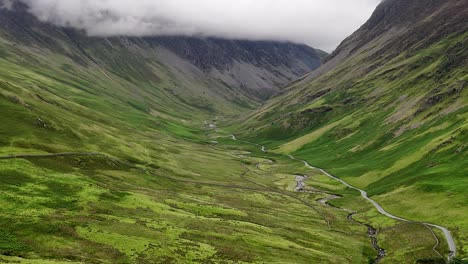 aerial footage of the Honister Pass in the Lake District National Park in Cumbria in the UK, a road and scenic valley. very green with clouds and mountain mist