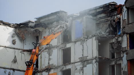 excavator long claw working in a dusty cloud. demolishing machinery destroys the roof of an old house. debris falling heavily from the roof.
