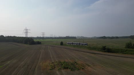 Drohnenaufnahmen-Eines-Zuges,-Der-Durch-Eine-Landschaft-Mit-Feldern-Auf-Beiden-Seiten-Der-Gleise-Fährt