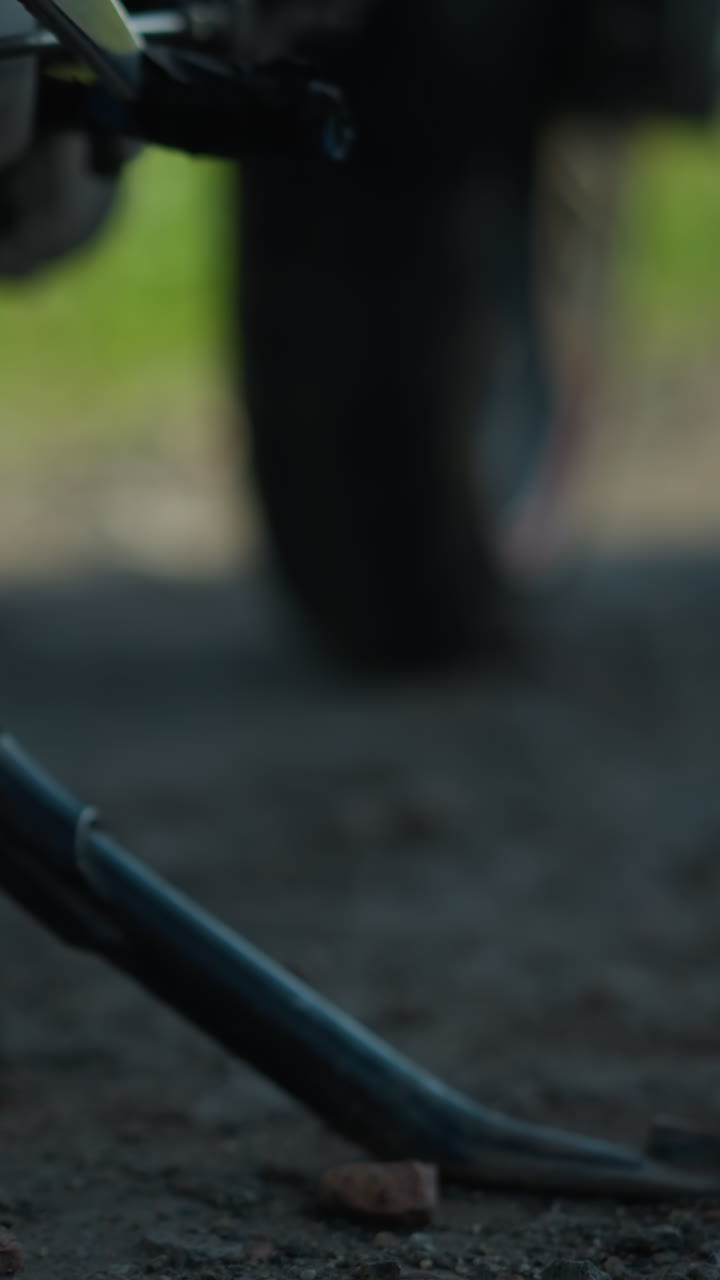 primer plano de un motociclista bajando el soporte de una motocicleta, con el neumático delantero girado a la izquierda y el fondo borroso