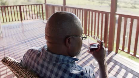 Hombre-Afroamericano-Mayor-Bebiendo-Vino-En-Una-Terraza-Soleada,-Cámara-Lenta