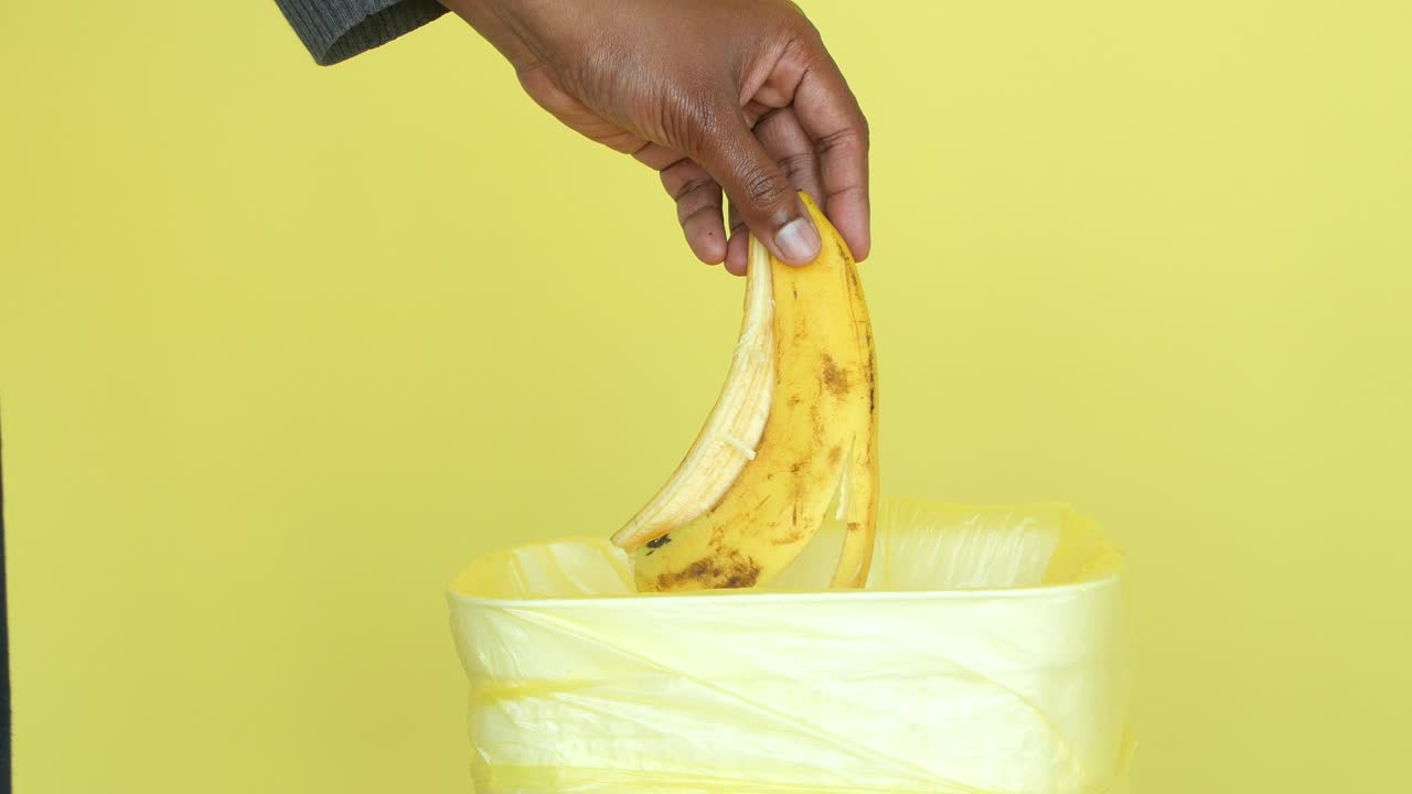 Mano che getta una buccia di banana in un cestino giallo