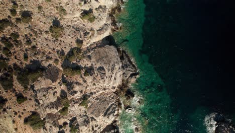 Drone-top-down-trucking-pan-along-rugged-rough-coastline-and-oceanic-drop-off-in-syros-greece