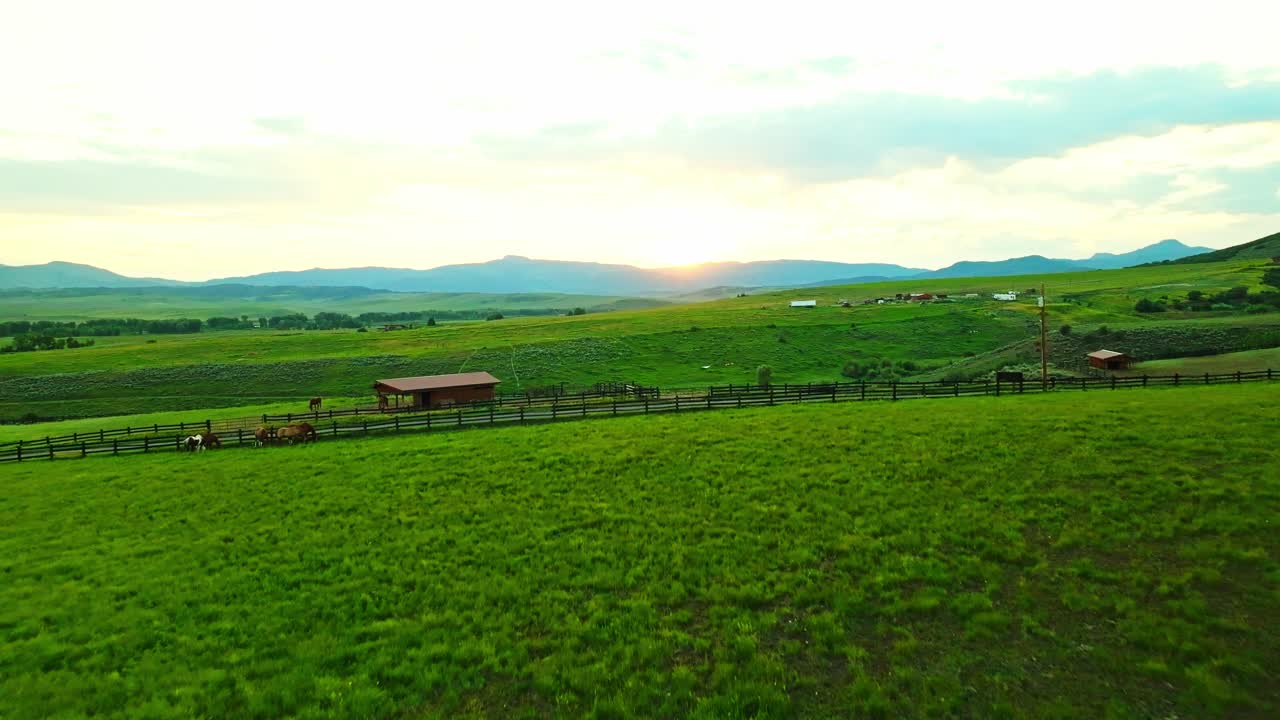 Low sun peeks through mountains at sunset in Steamboat Springs, golden light silhouettes of horses grazing and sweeping farmlands
