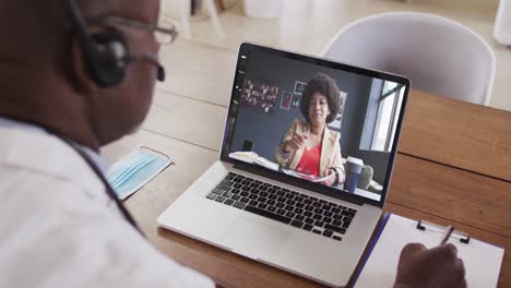 african american businessman sitting at desk using laptop having video call with female colleague