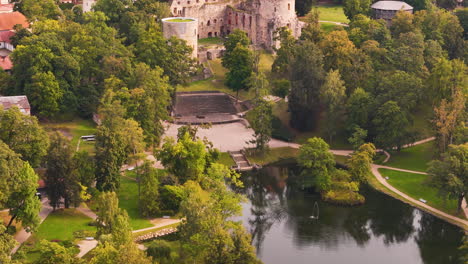 drone footage of cesis medieval castle ruins, lush greenery, and a tranquil pond in latvia.