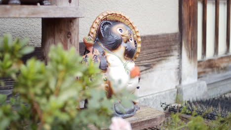 green leaves, tanuki, racoon statue sittng outside a house in kyoto, japan soft lighting